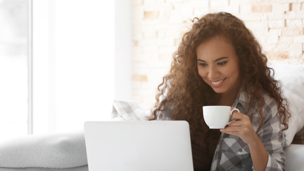 Woman with curly hair doing niche market research for her small business while drinking coffee